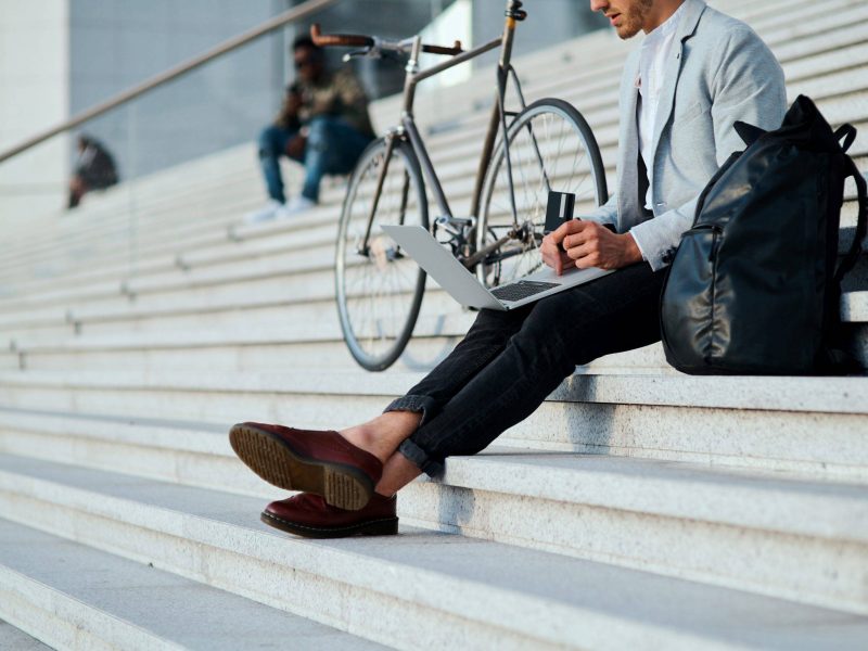 Shot of a young businessman using a laptop and credit card on the steps in a city